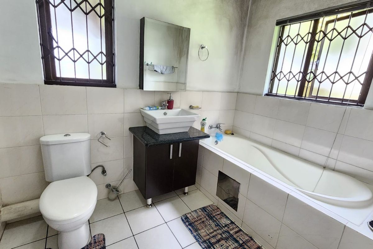 A functional bathroom featuring a vessel sink with vanity, built-in bathtub, and tiled finishes, requiring cosmetic updates to address wall staining and general wear.