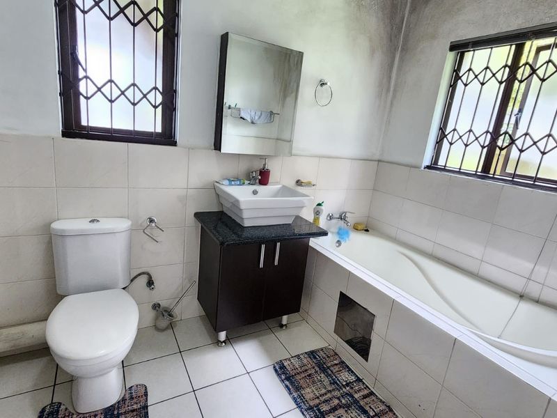 A functional bathroom featuring a bathtub, vessel sink with vanity cabinet, and toilet, with visible signs of moisture damage on the upper wall and ceiling.