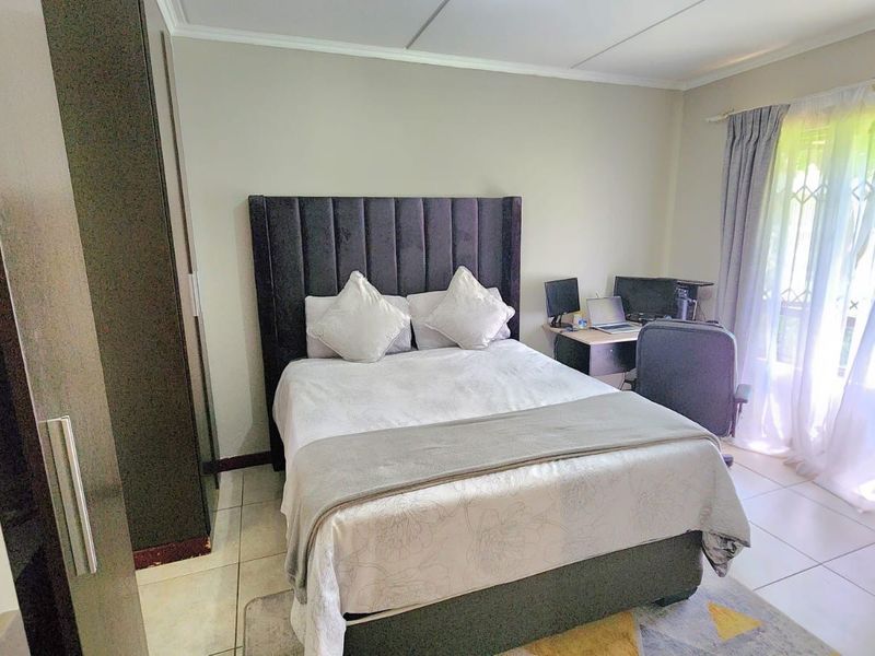 A functional bedroom featuring tiled flooring, a built-in wardrobe, and natural light through a window with security gate.