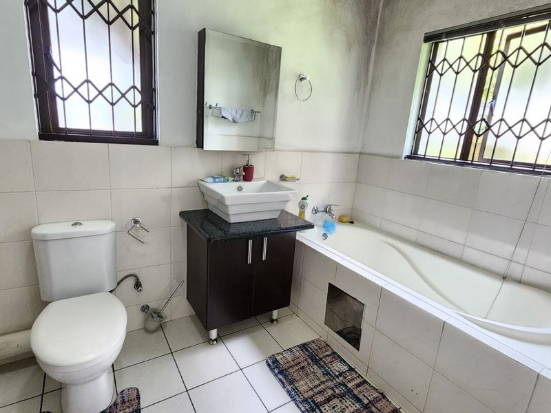 A functional bathroom featuring a vessel sink with vanity, built-in bathtub, and tiled finishes, requiring cosmetic updates to address wall staining and general wear.