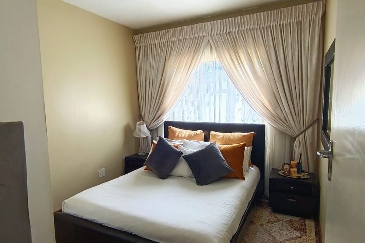 A compact bedroom featuring tiled flooring, neutral wall tones, and a window dressed with floor-to-ceiling curtains.