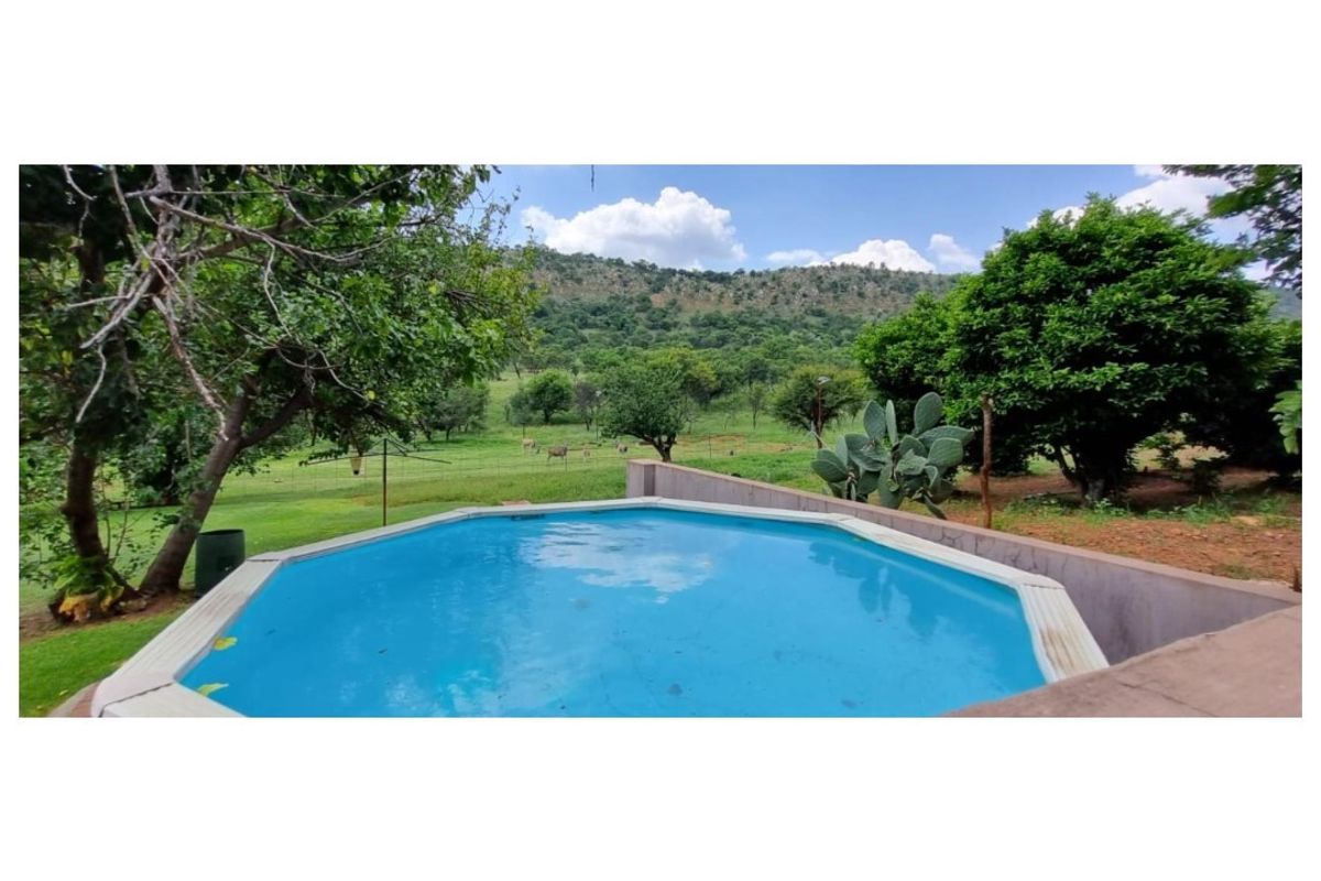An above-ground swimming pool set within a rural landscape, featuring a retaining wall and scenic views of the surrounding hills and greenery.