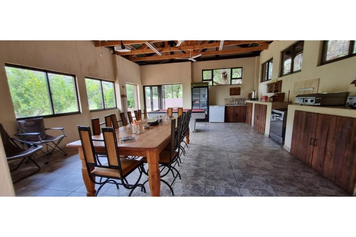 Spacious open-plan entertainment area featuring exposed timber trusses, tiled flooring, and a functional kitchen section with built-in cabinetry and stainless steel appliances.
