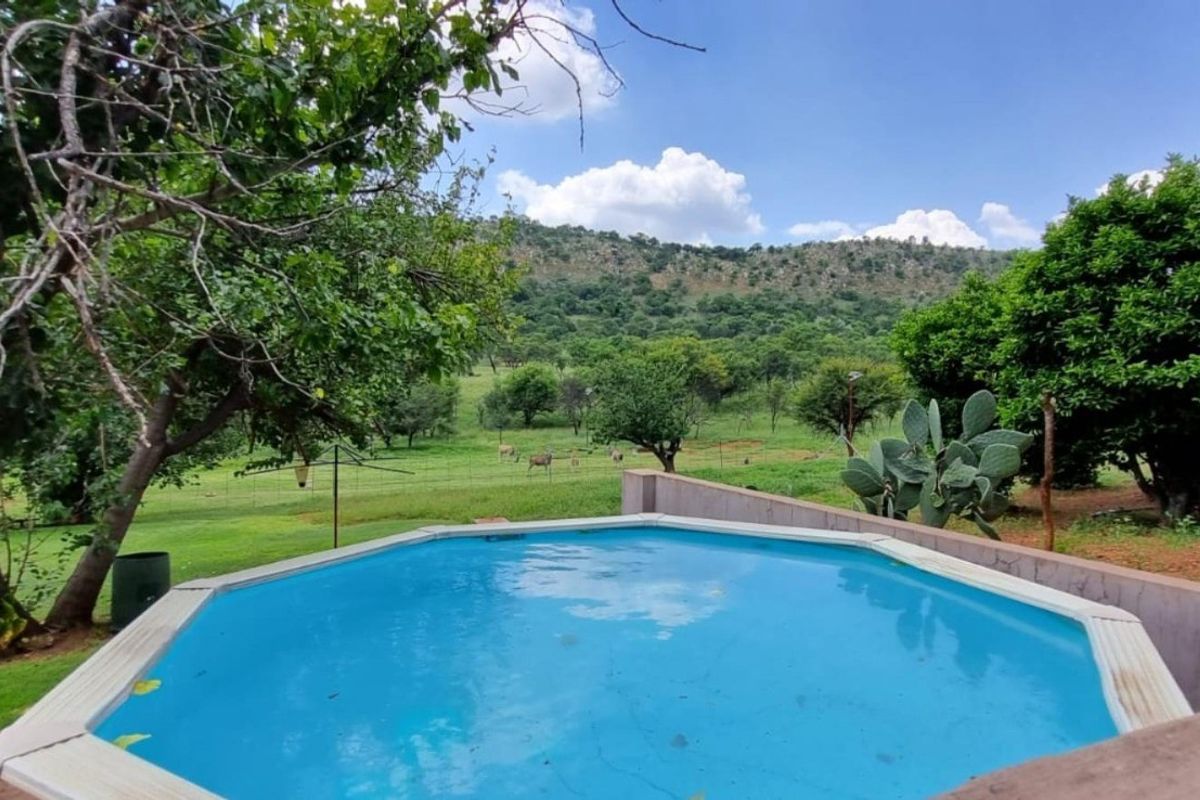 An above-ground swimming pool set within a lush garden landscape, featuring scenic views of the surrounding hills and natural farm terrain.