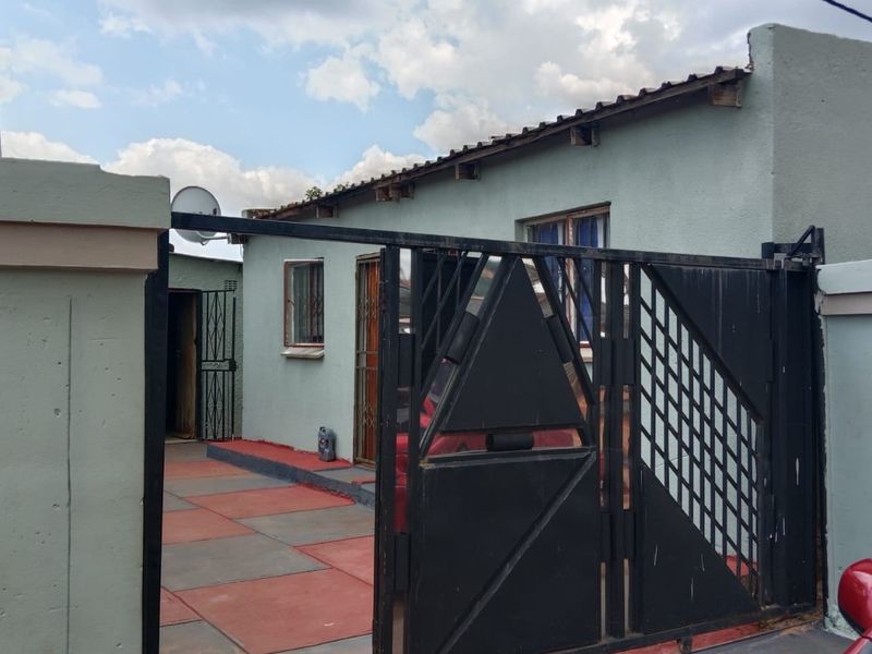 Front exterior view of the property featuring a metal security gate, paved driveway, and perimeter walling.