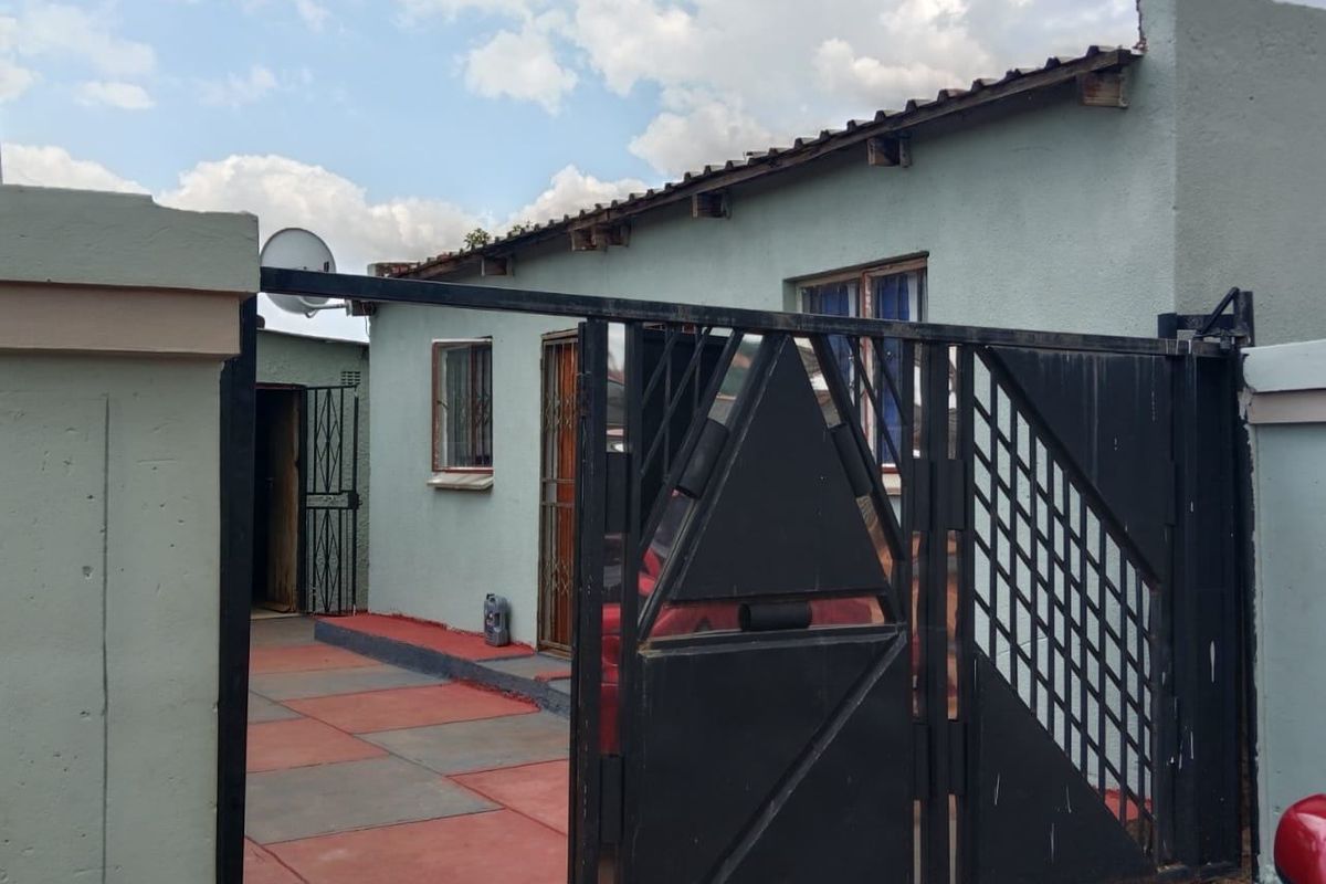 Front exterior view of the property featuring a metal security gate, paved driveway, and perimeter walling.