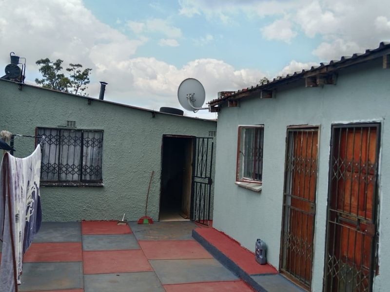 Rear courtyard area featuring paved flooring, security gates on doorways, and security bars on windows, with visible wear to the exterior building finishes.