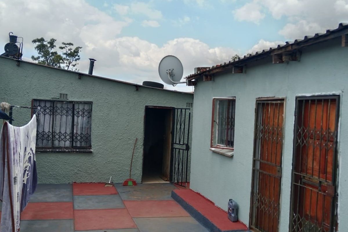 Rear courtyard area featuring paved flooring, security gates on doorways, and security bars on windows, with visible wear to the exterior building finishes.
