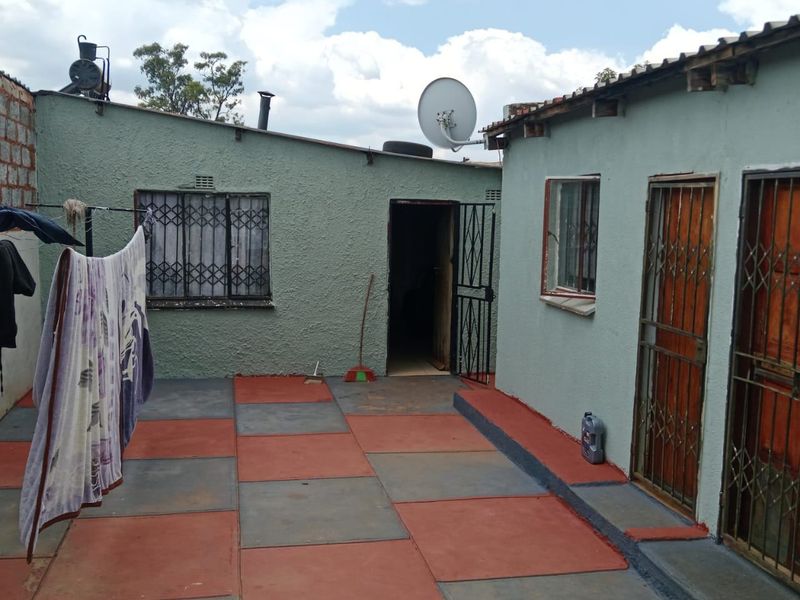 Rear courtyard area featuring paved flooring, security gates on doorways, and security bars on windows, providing access to the main dwelling structure.