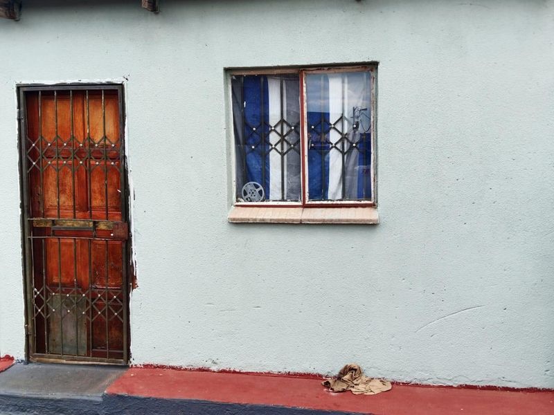 Exterior view of a residential building facade featuring a wooden door with a security gate and a window with security bars.