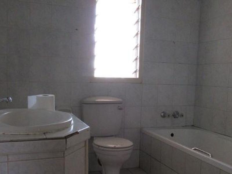 A dated bathroom featuring a tiled vanity, standard toilet, and bathtub with full-height wall tiling and a louvre window.