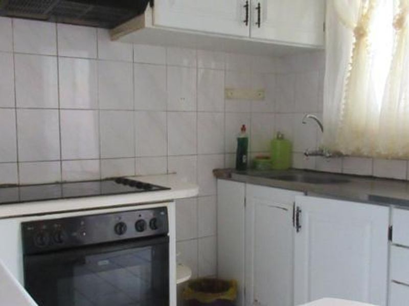 A functional kitchen featuring white cabinetry, a built-in oven with electric hob, extractor fan, and tiled backsplash with a stainless steel sink.