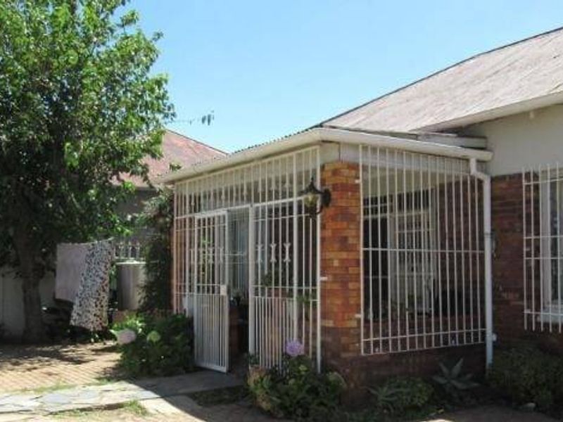 Rear exterior view of the house featuring a paved patio area, brick facade, and security bars on windows and the covered porch.