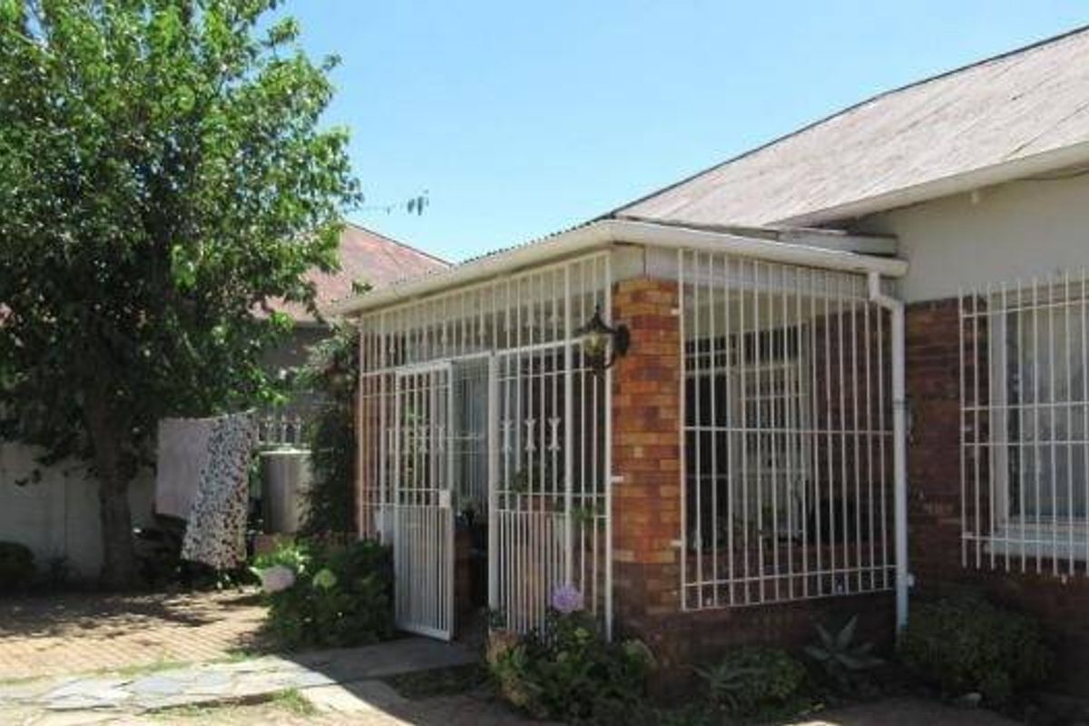 Rear exterior view of the house featuring a paved patio area, brick facade, and security bars on windows and the covered porch.