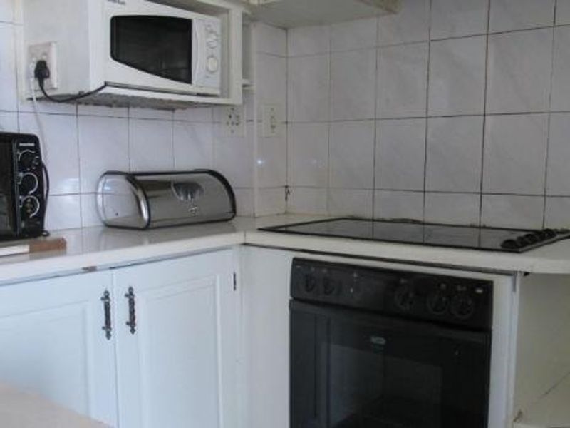 A compact kitchen featuring built-in cabinetry, an integrated oven, and an electric hob with tiled wall finishes.