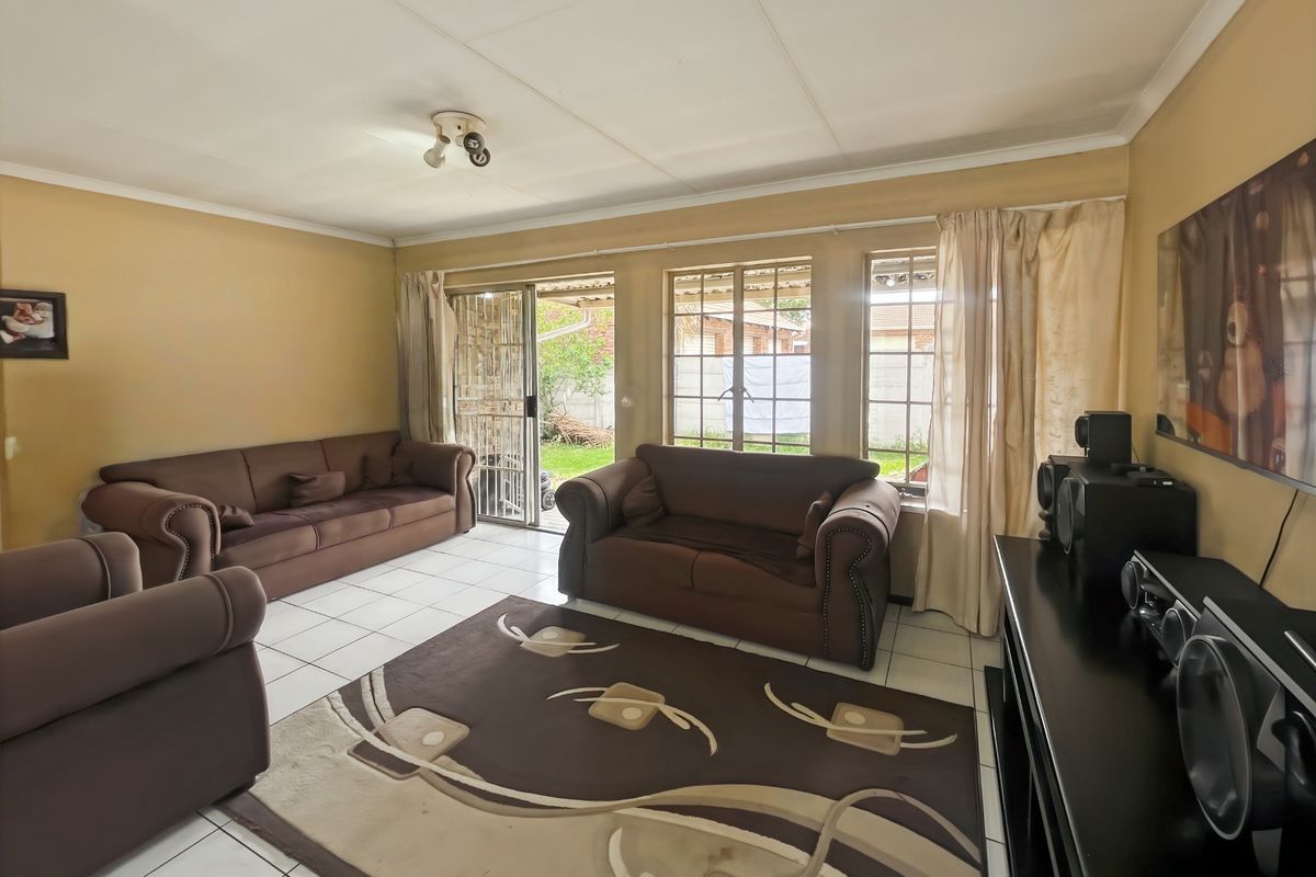 A living room featuring tiled flooring, large windows, and a sliding door providing access to the rear garden area.