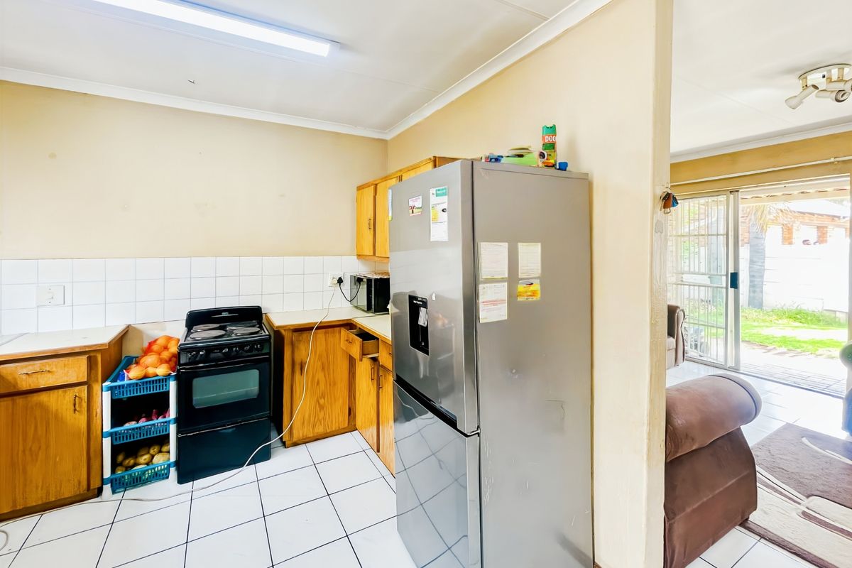 A functional kitchen featuring wooden cabinetry, tiled flooring, and a tiled splashback, adjacent to an open-plan living area with access to the patio.