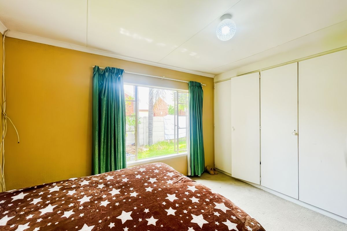 A bedroom featuring built-in cupboards and a large window providing natural light, offering a functional space ready for a modern update.
