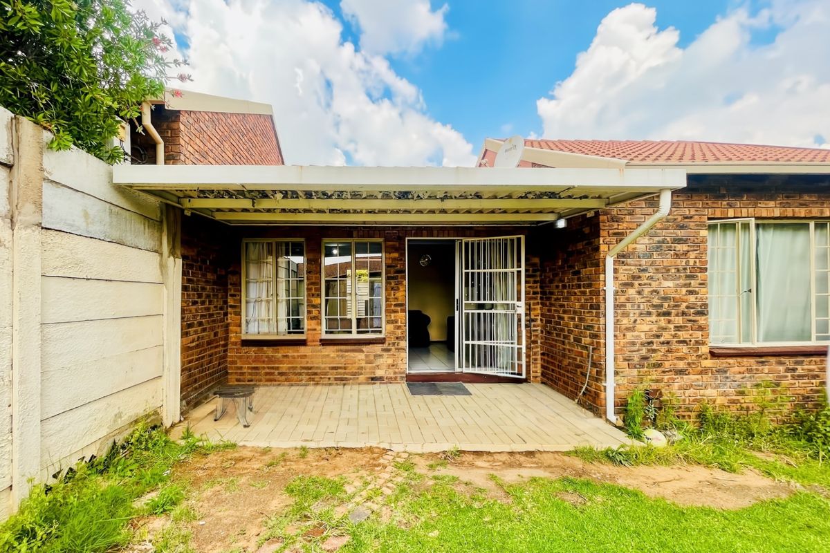 Rear exterior view of a brick townhouse featuring a covered patio area, security gate, and a small garden space.