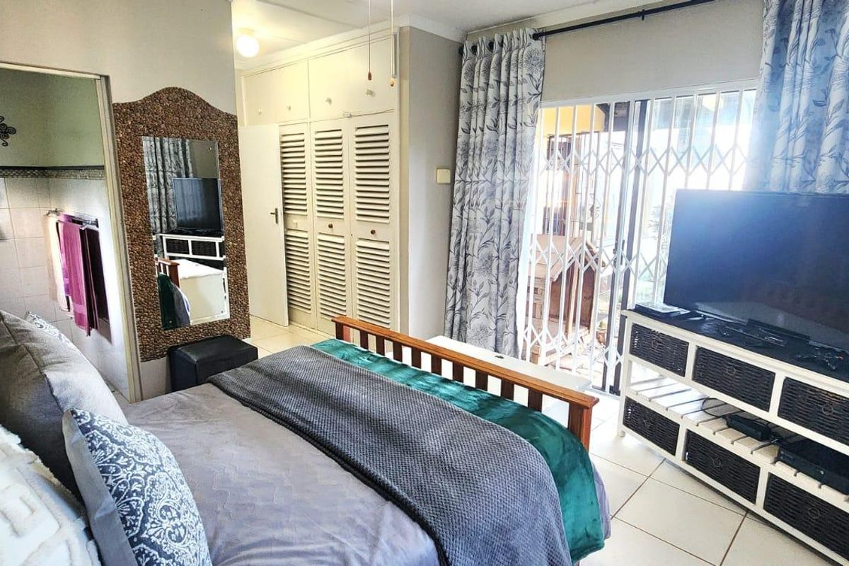 A bedroom featuring built-in cupboards, tiled flooring, and a sliding glass door with security gate leading to an outdoor area, with an attached en-suite bathroom.