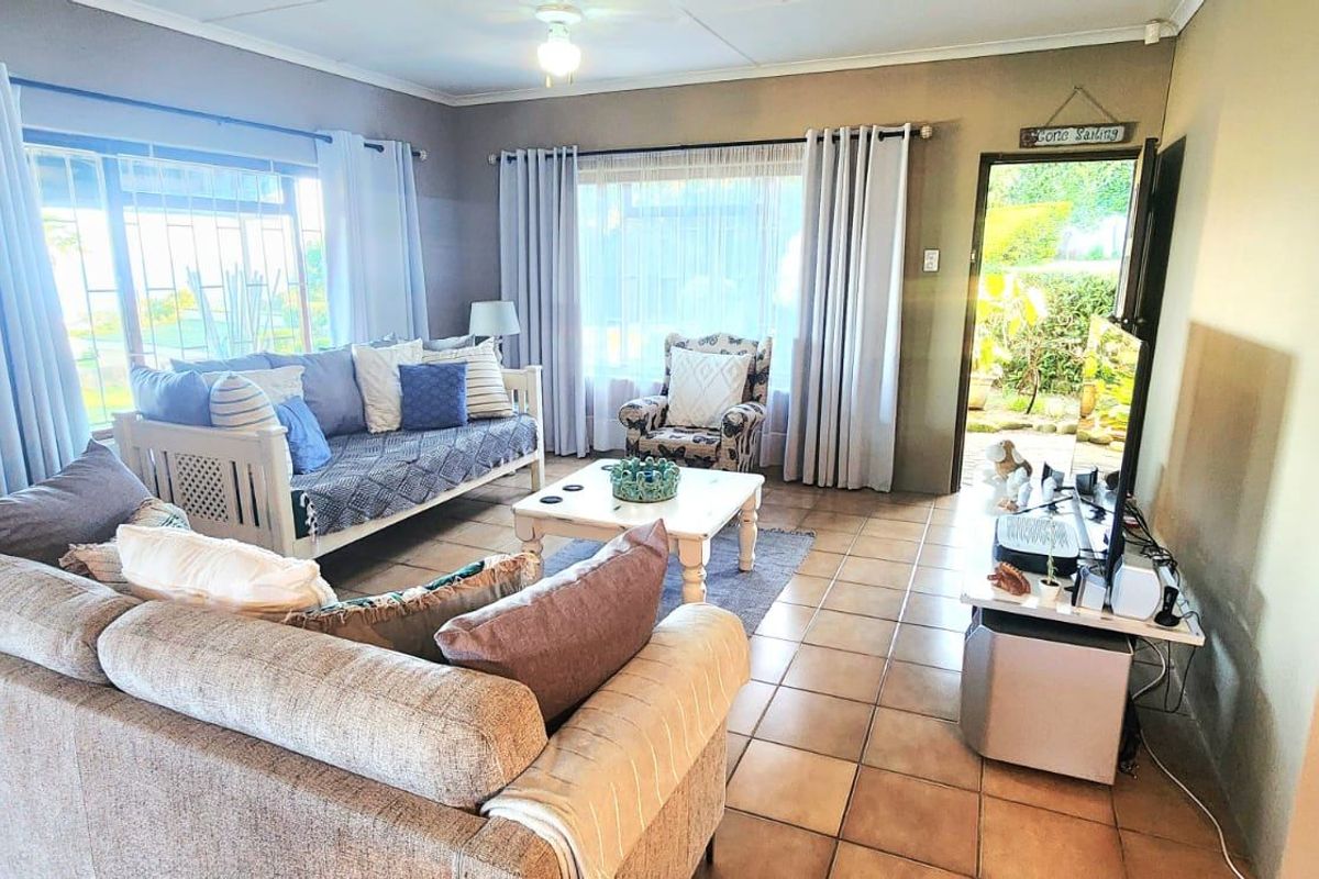 A comfortable living room featuring tiled flooring, a ceiling fan, and large windows that provide natural light and access to the outdoor area.
