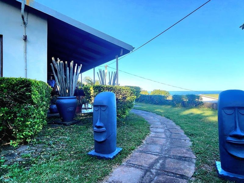 A rear garden view featuring a stone pathway leading to a covered patio area with a view of the surrounding landscape.