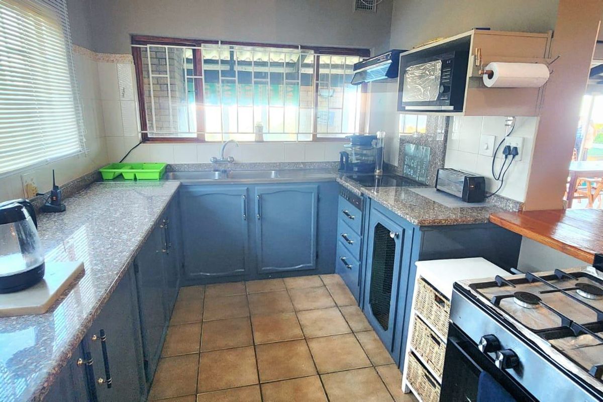 Functional kitchen featuring blue cabinetry, laminate countertops, double basin sink, and tiled flooring with security bars on the window.