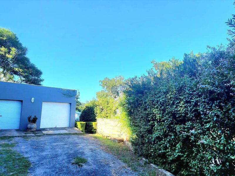 A detached double garage with roller doors, situated at the end of a concrete driveway, surrounded by established garden greenery.