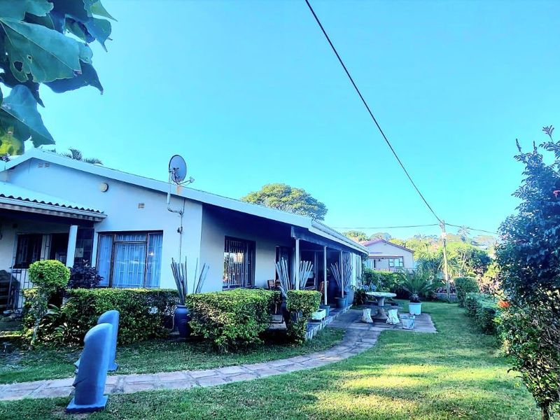 Rear view of the house featuring a covered patio, paved garden walkway, and established landscaping.