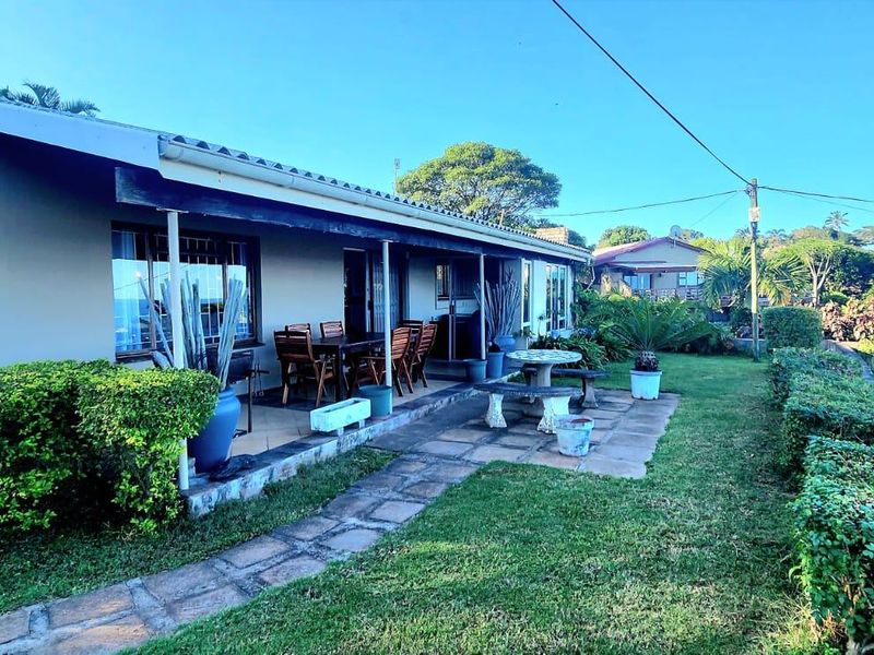 Rear view of the property featuring a covered patio area, paved walkway, and established garden with mature landscaping.