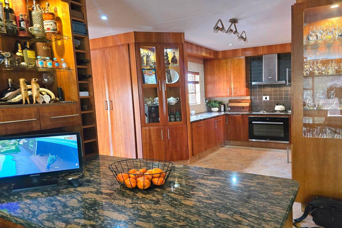 A well-maintained kitchen featuring extensive wooden cabinetry, granite countertops, built-in oven, hob, and integrated glass display shelving.