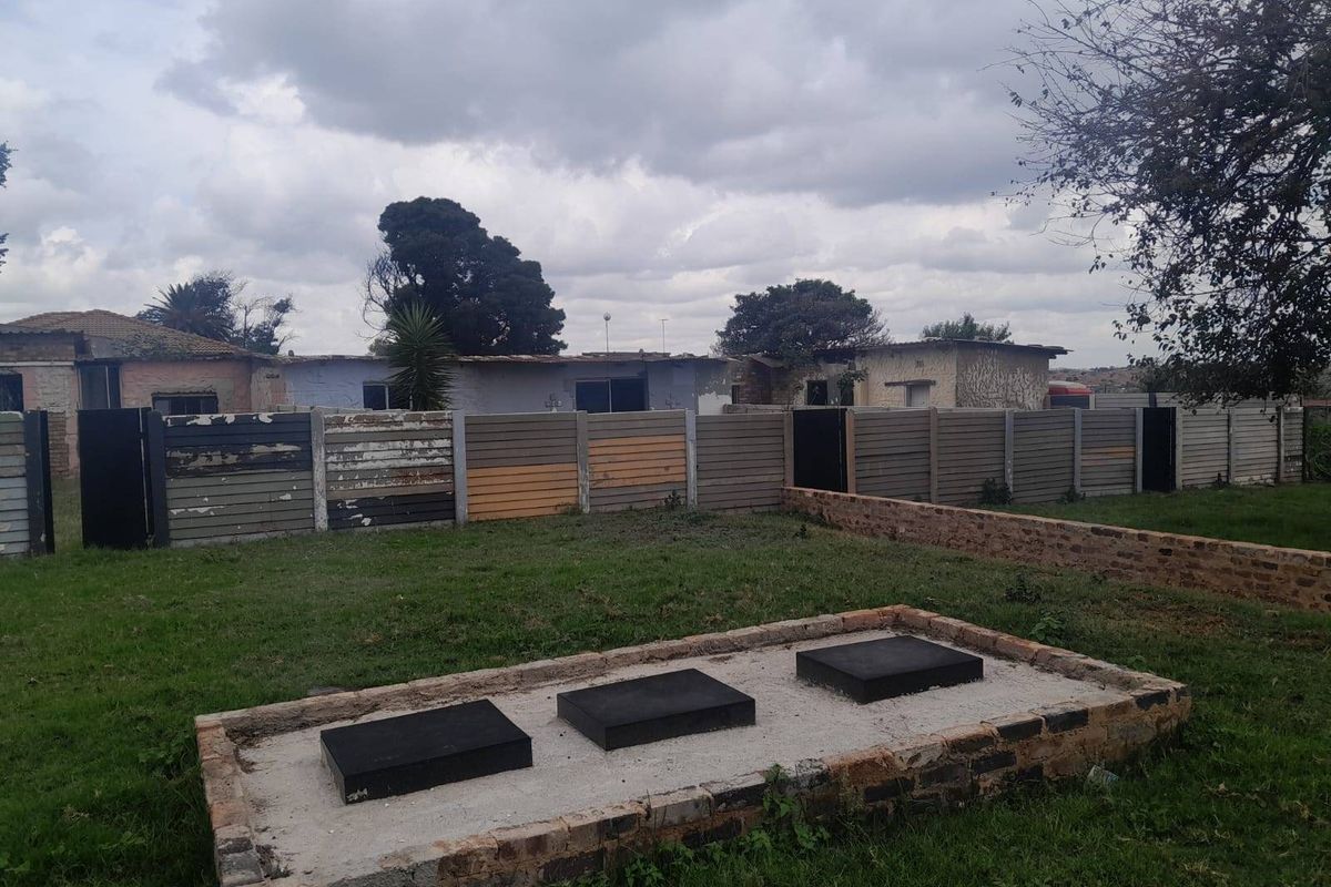 Rear garden area featuring a lawn, a brick-edged concrete platform, and a precast concrete boundary wall showing signs of weathering.