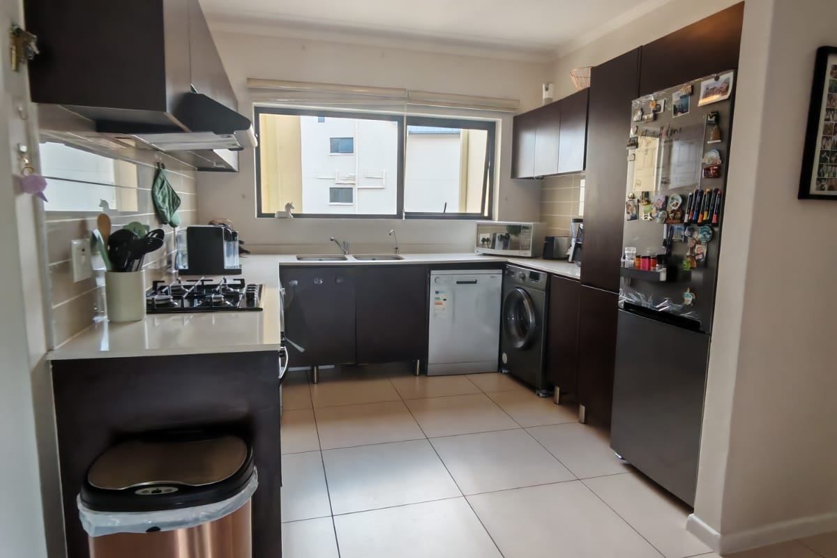 A functional kitchen featuring dark cabinetry, a gas hob, integrated appliances, and tiled flooring with ample counter space.