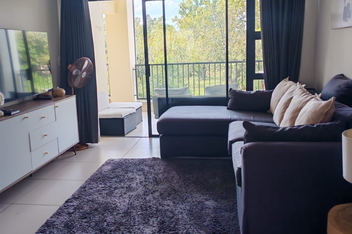 A well-maintained living room featuring large format floor tiles and a sliding glass door providing access to an outdoor balcony area.