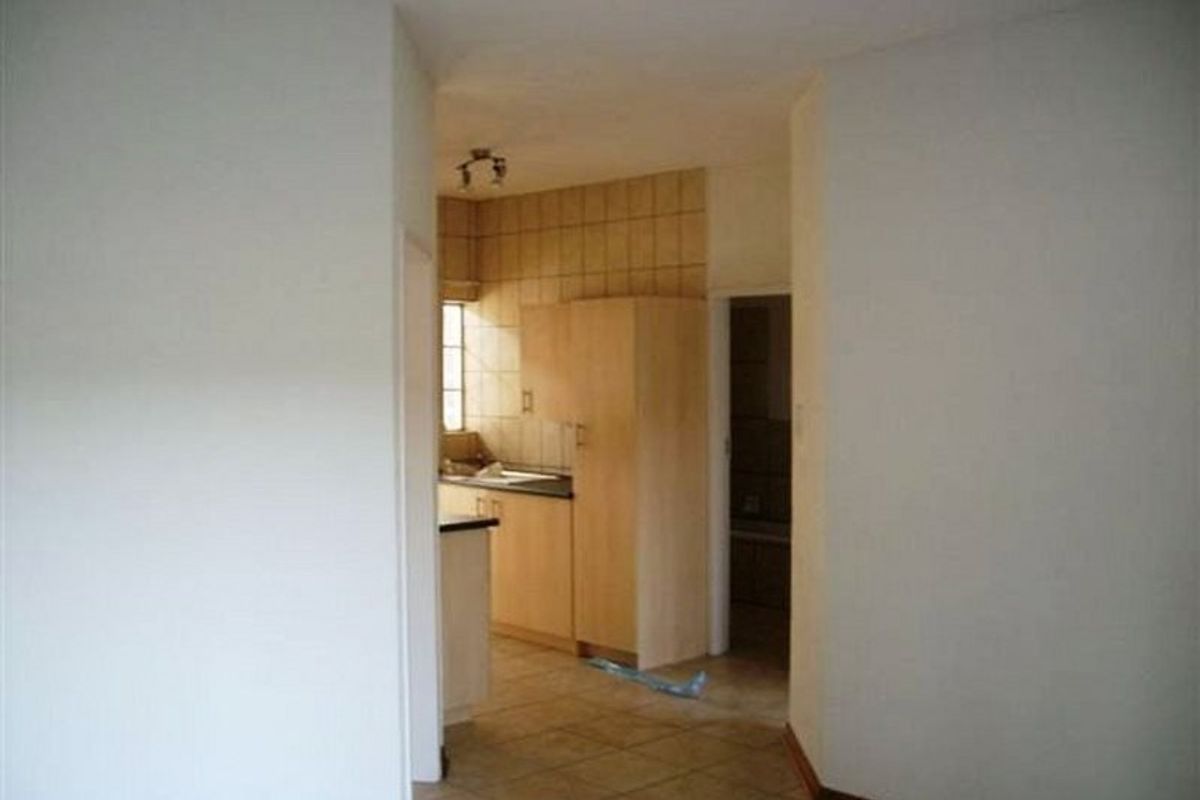 A view from a hallway looking into a functional kitchen area featuring light wood cabinetry and tiled splashbacks.