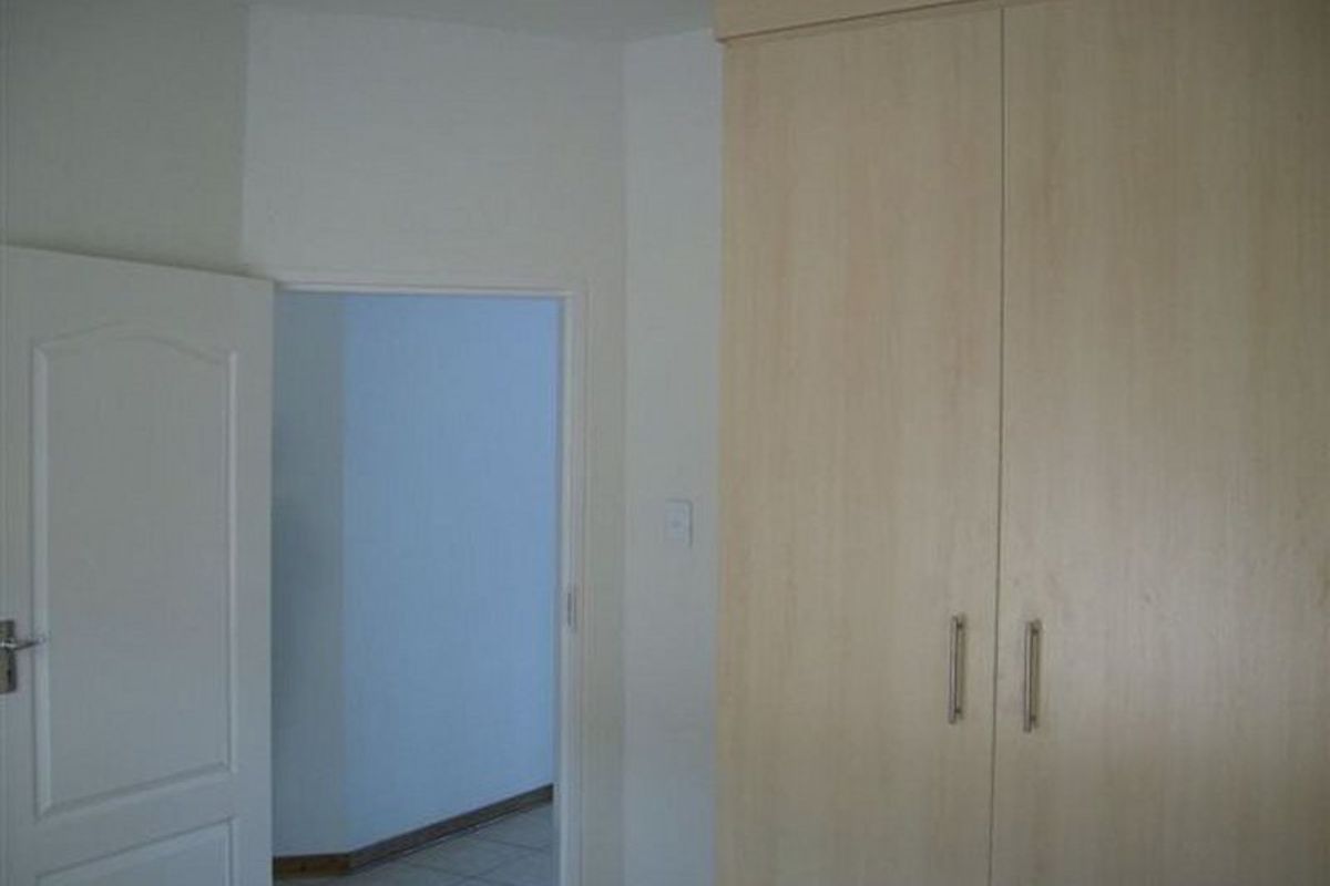 A bedroom interior featuring built-in light wood cabinetry and a doorway leading to an adjacent tiled hallway.