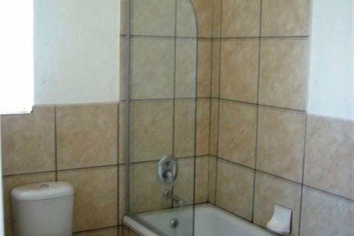 A functional bathroom featuring a bathtub with a glass shower screen, a standard toilet, and a pedestal sink with neutral wall tiling.