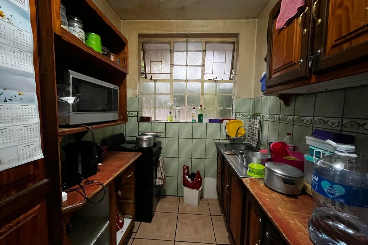 A compact, dated kitchen featuring timber cabinetry, tiled splashbacks, and a functional layout with a stainless steel sink and freestanding stove.