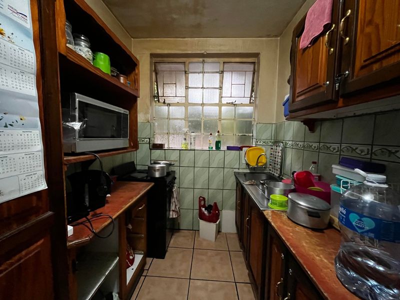 A compact, dated kitchen featuring timber cabinetry, tiled splashbacks, and a functional layout with a stainless steel sink and freestanding stove.
