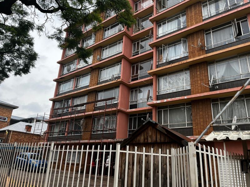 Exterior view of a multi-story apartment building featuring brick facade, metal window frames, and perimeter security fencing.