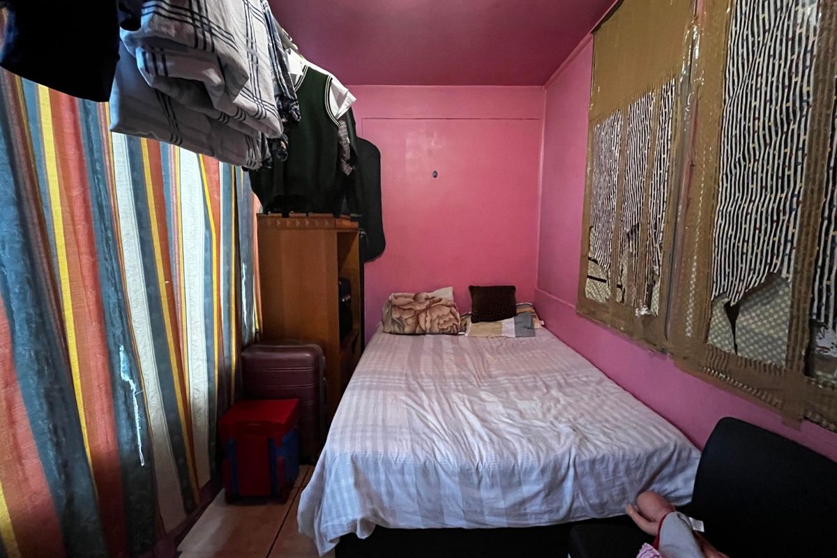 A compact bedroom featuring tiled flooring and pink painted walls, currently used as a multi-purpose living and storage space.