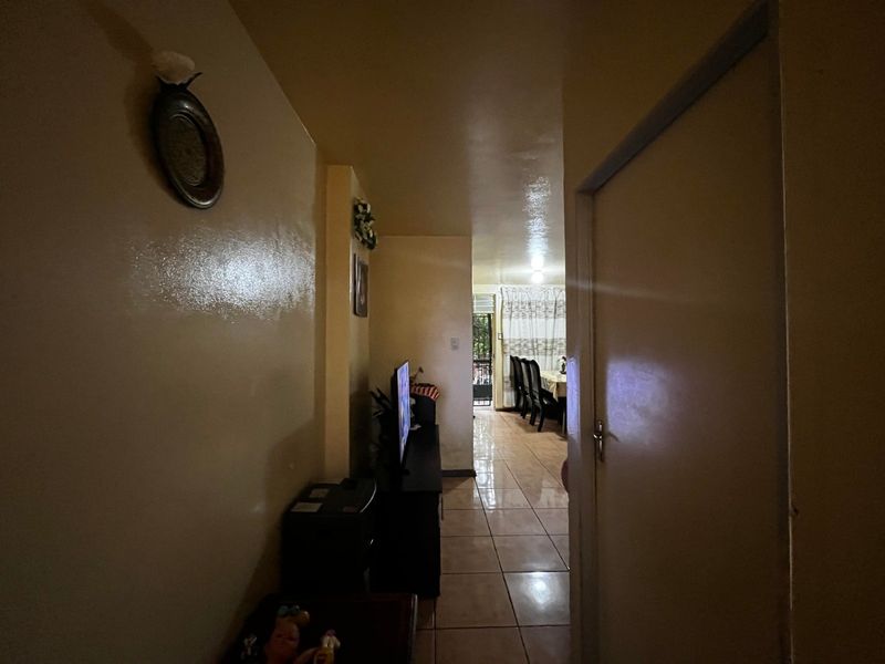 A view through a hallway leading into an open plan living and dining area with tiled flooring throughout.