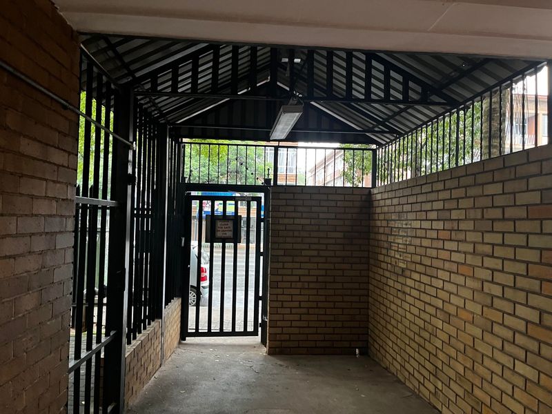 A secure, covered entrance area featuring brick walls, a metal security gate, and a pitched metal roof structure.