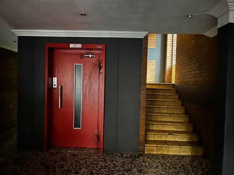 A communal apartment hallway featuring a red elevator door, brick wall accents, and a tiled staircase leading to the upper level.
