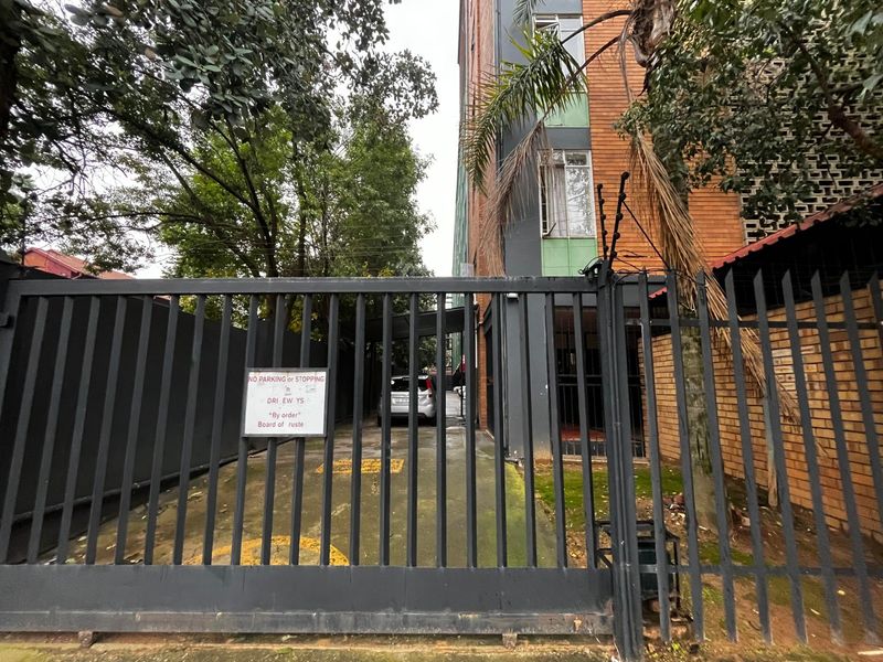 Front entrance view of the apartment complex featuring a secure metal gate, electric fencing, and a paved driveway.