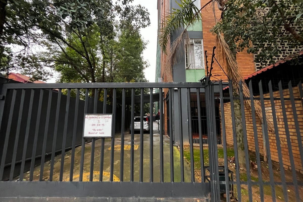 Front entrance view of the apartment complex featuring a secure metal gate, electric fencing, and a paved driveway.