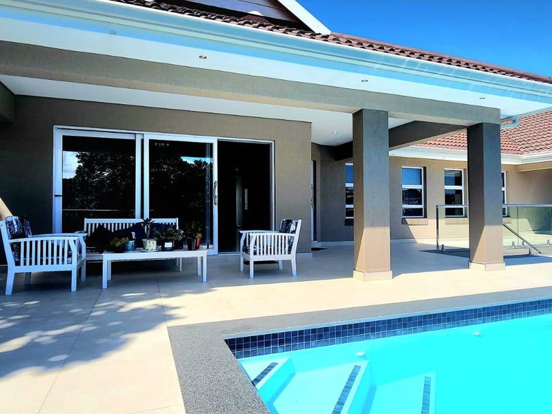 A spacious covered patio overlooking a swimming pool, featuring modern tiled flooring, glass balustrades, and direct access to the home via sliding doors.
