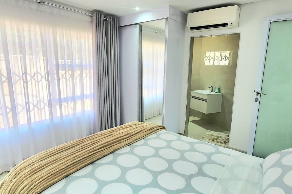A well-maintained bedroom featuring a built-in wardrobe, split-system air conditioning, and an attached en-suite bathroom with modern fixtures.