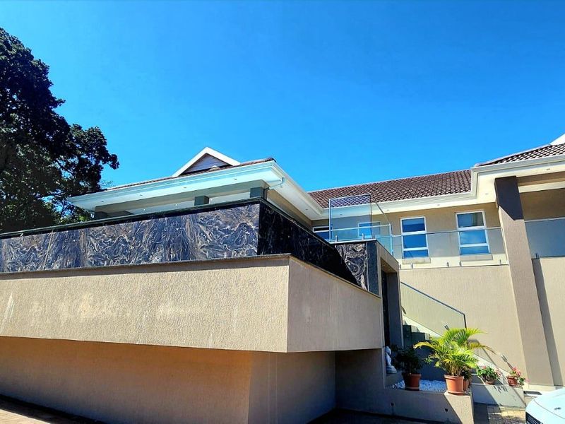 Modern multi-level residential facade featuring stone cladding, glass balustrades, and a paved driveway under a clear blue sky.
