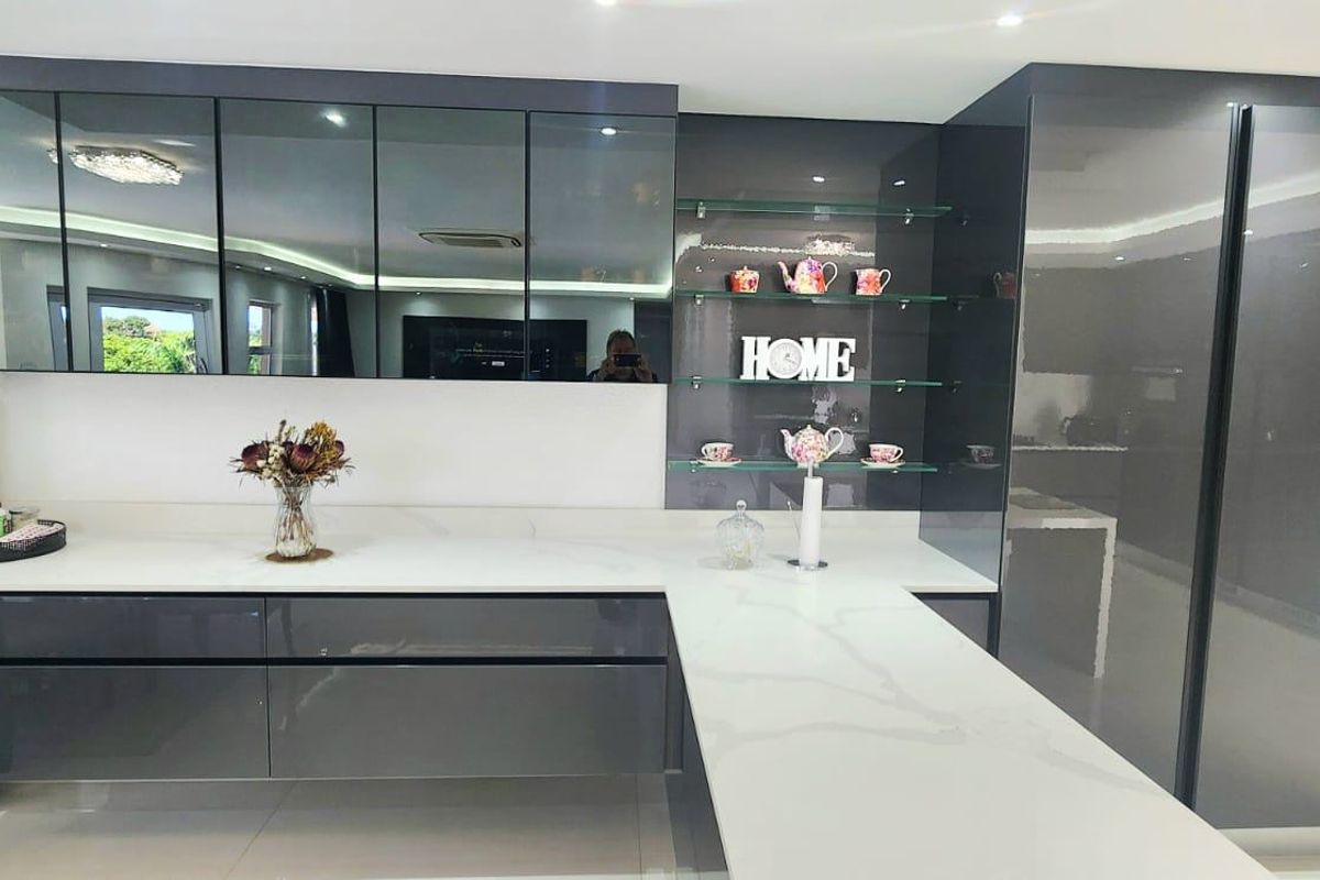 Modern kitchen featuring high-gloss grey cabinetry, white stone countertops, and integrated storage with sleek glass shelving.